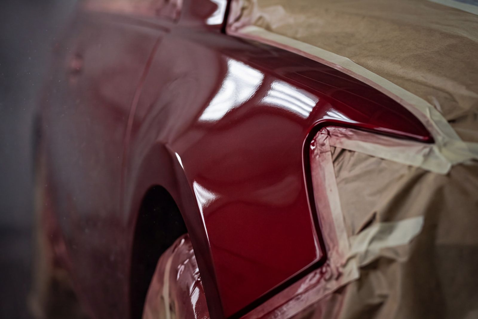 Aile arrière rouge fraîchement vernie dans une cabine de peinture, le reste du véhicule masqué